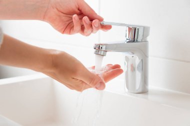 Kadın musluğu açıp su ısısını denerken afiş. Krom musluktan su akıyor. Banyo tesisatı. Vücut bakımı ve hijyen
