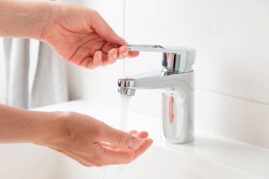 Doğal kaynakların sürdürülebilir kullanımı. Kadın su musluğunu açıp kapıyor. Krom musluktan su akıyor. Su kaynakları kavramını, çevre koruma kavramını kullanarak