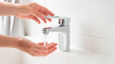 Kadın pankartı su akışı musluğunu açıp kapıyor ve su sıcaklığını dolduruyor. Krom musluktan su akıyor. Banyo tesisatı. Su kaynakları kavramını kullanarak