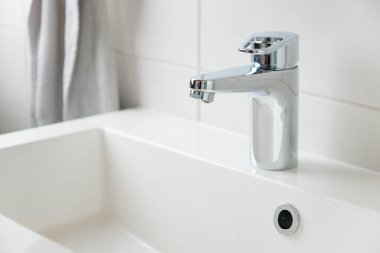 Beyaz modern banyodaki musluktan damlayan bir damla saf su. Temiz musluk suyu konsepti. Doğal kaynakların akıllıca kullanımı.