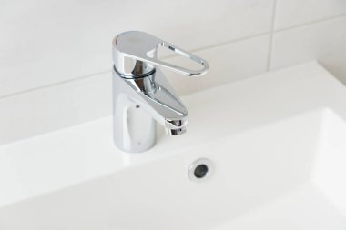 Beyaz modern banyodaki musluktan damlayan bir damla saf su. Temiz musluk suyu konsepti. Doğal kaynakların akıllıca kullanımı.