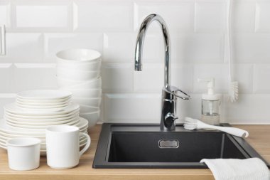 Temiz sofra takımı. Bulaşık yıkama kavramı. Bulaşık deterjanı, fırça, tabak ve bardaklar siyah mutfak lavabosunun yanında, ahşap tezgahta krom musluk ve beyaz metro döşemesi.