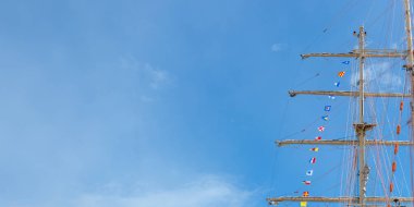 Uluslararası denizcilik bir bayrak direğinde bayraklar ve arkasında mavi bir gökyüzü olan yelkenli bir gemide direkler. Pankart