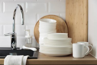 Temiz sofra takımı. Bulaşık yıkama kavramı. Bulaşık deterjanı, fırça, tabak ve bardaklar siyah mutfak lavabosunun yanında, ahşap tezgahta krom musluk ve beyaz metro döşemesi.