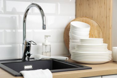 Temiz sofra takımı. Bulaşık yıkama kavramı. Bulaşık deterjanı, fırça, tabak ve bardaklar siyah mutfak lavabosunun yanında, ahşap tezgahta krom musluk ve beyaz metro döşemesi.