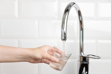 İnsan eli bardakları, beyaz mutfaktaki musluk suyuyla doldurur. Doğal temiz su konseptiyle pankart, fotokopi alanı ile pankart.