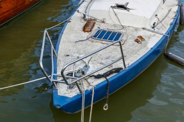 Denizde terk edilmiş, eski, kirli, bakımsız bir yelkenlinin kapısına yakın açık mavi ve beyaz yelkenli, kırık direkli.