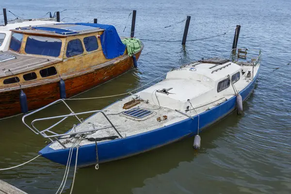 Denizde terk edilmiş, eski, kirli, bakımsız bir yelkenlinin kapısına yakın açık mavi ve beyaz yelkenli, kırık direkli.