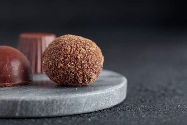 Premium gourmet chocolate handmade truffles from confectionery, homemade dark chocolate candies on marble plate and black background