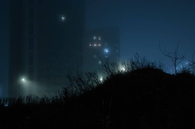 Şehirde sisli bir gece, aydınlık sokak lambaları, sisli gökyüzünün ve Finlandiya 'da yoğun sislerin arasında gizlenmiş çimen tepesinin arka planında yüksek binalar, Espoo