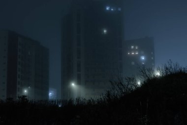 Şehirde sisli bir gece, aydınlık sokak lambaları, sisli gökyüzünün ve Finlandiya 'da yoğun sislerin arasında gizlenmiş çimen tepesinin arka planında yüksek binalar, Espoo