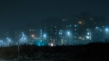 Şehirde sisli bir gece, aydınlık sokak lambaları, sisli gökyüzünün ve Finlandiya 'da yoğun sislerin arasında gizlenmiş çimen tepesinin arka planında yüksek binalar, Espoo
