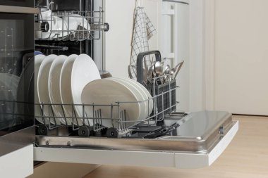 Kapısı açık, bulaşık makinesi temiz bulaşıklarla dolu, beyaz çatal bıçak. Modern teknolojiler ev mutfağında minimalist dolap şiirleriyle. Günlük ev işleri basitleştiriliyor.