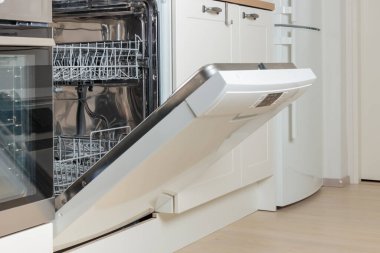 Kapısı açık, bulaşık makinesi temiz bulaşıklarla dolu, beyaz çatal bıçak. Modern teknolojiler ev mutfağında minimalist dolap şiirleriyle. Günlük ev işlerini basitleştirmek, sürdürülebilirlik ve çevre dostu yaşam, akıllı ev ve otomasyon