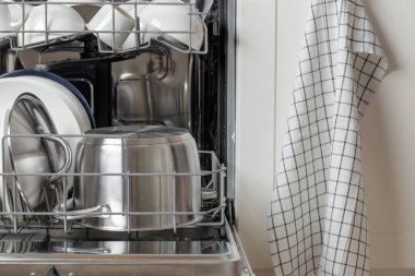 Kapısı açık bir bulaşık makinesinde temiz tabaklar, beyaz bir kap kacak ve paslanmaz çelik bir su ısıtıcı bulunur. Ev mutfağında minimalist kabine şiirleriyle modern teknolojiler günlük ev işlerini basitleştiriyor