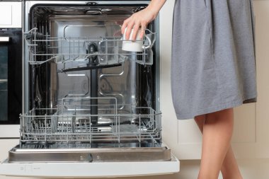 Kadın eli bulaşık makinesini sofra takımıyla dolduruyor. Mutfak aletleri, yaşam tarzı manzarası. Kadın bulaşık makinesinden bir bardak alıyor. Mutfaktaki modern teknoloji kavramı
