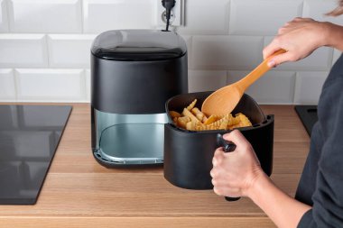 Evde moda mutfak gereçleri kullanan bir kadın. Havalandırma makinesi. Kızarmış patates, küçük tezgah konveksiyon fırını.