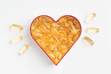 Beyaz zemin üzerinde Omega 3 veya D vitamini içeren sarı kapsüllerden yapılmış kalp. Balık yağından sarı haplar. Kalp hastalığı ve iskemik felci önlüyor. Cilt bakımı, depresyon tedavisi