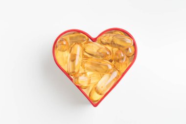 Beyaz zemin üzerinde Omega 3 veya D vitamini içeren sarı kapsüllerden yapılmış kalp. Balık yağından sarı haplar. Kalp hastalığı ve iskemik felci önlüyor. Cilt bakımı, depresyon tedavisi