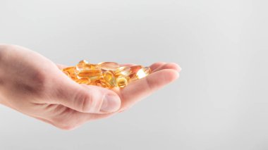 Elinde sarı Omega 3 vitamini ya da beyaz arka planda D jel kapsülleri var. Balık yağından sarı haplar. Kalp hastalığı ve iskemik felci önlüyor. Cilt bakımı, depresyon tedavisi