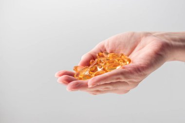 Elinde sarı Omega 3 vitamini ya da beyaz arka planda D jel kapsülleri var. Balık yağından sarı haplar. Kalp hastalığı ve iskemik felci önlüyor. Cilt bakımı, depresyon tedavisi