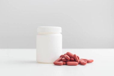 Kırmızı haplar ve plastik ilaç şişesi beyaz arka planda fotokopi alanı ile birlikte. İlaç ve sağlık kavramları arasında Ferrum, demir hapları veya Fe vitamini içeren bir kavanoz vardır. Yüksek kaliteli fotoğraf modeli.