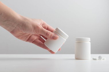 Genç bir kadının eli beyaz arka planda beyaz bir plastik şişe alır. Kutuyu haplarla, kapsüllerle, haplarla, ilavelerle ya da vitaminlerle damgalamak için bir model. Sağlık hizmetleri kavramı