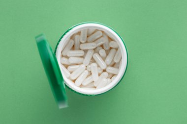Beyaz plastik kapsül şişesi ve yeşil kapak. İlaçlı hastalıkların tedavisi için tıbbi konsept. Vitaminler, her gün için haplar veya antibiyotikler. Yeşil arkaplanda üst görünüm.