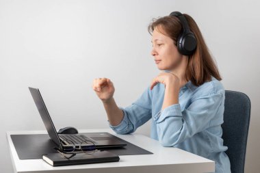 Kulaklıklı, dizüstü bilgisayar kullanan sakin bir kadın bilgisayar ekranına bakıyor. Uzaktan kumandalı, çalışkan, evden çalışıyor. Doğru duruş, iyi ortam