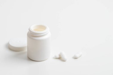 Beyaz haplar ve plastik ilaç şişesi beyaz arka planda fotokopi alanı ile. İlaç ve sağlık konseptleri içinde haplar veya vitaminler olan bir kavanoz içerir. Yüksek kaliteli fotoğraf maketi afişi