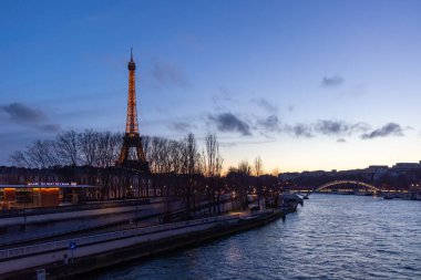 Paris, Fransa - 24 Şubat 2025: Aydınlatılmış Eyfel Kulesi ve Paris, Fransa 'daki Seine nehri üzerindeki Pont Debilly Footbridge' in gece manzarası