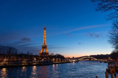 Paris, Fransa - 24 Şubat 2025: Aydınlatılmış Eyfel Kulesi ve Paris, Fransa 'daki Seine nehri üzerindeki Pont Debilly Footbridge' in gece manzarası