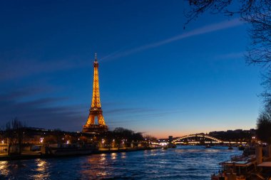 Paris, Fransa - 24 Şubat 2025: Aydınlatılmış Eyfel Kulesi ve Paris, Fransa 'daki Seine nehri üzerindeki Pont Debilly Footbridge' in gece manzarası