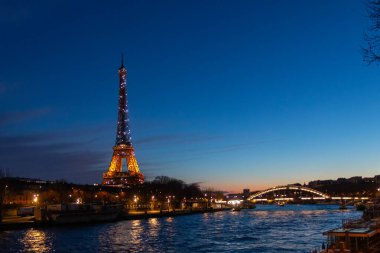 Paris, Fransa - 24 Şubat 2025: Aydınlatılmış Eyfel Kulesi ve Paris, Fransa 'daki Seine nehri üzerindeki Pont Debilly Footbridge' in gece manzarası