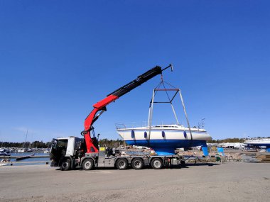 Suomenoja, Espoo, Finlandiya 'da bir limanda vinç tarafından bir yelkenli kaldırılıyor. Ağır kaldırma kayışlarıyla havada asılı kalan gemi bakım ve mevsimsel depolama için hareket ediyor.