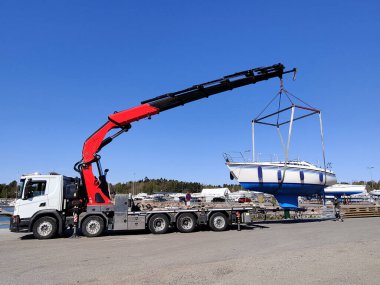 Finlandiya, Espoo 'daki Suomenoja limanında vinç tarafından çalınan bir yelkenli. Bir adam bir halat tutuyor, kayışı kaldırarak havada asılı duran tekneye rehberlik ediyor.