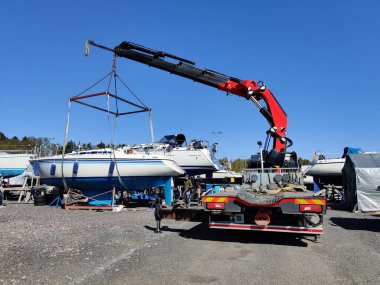 Finlandiya, Espoo 'daki Suomenoja limanında vinç tarafından çalınan bir yelkenli. Bir adam bir halat tutuyor, kayışı kaldırarak havada asılı duran tekneye rehberlik ediyor.