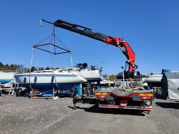 Finlandiya, Espoo 'daki Suomenoja limanında vinç tarafından çalınan bir yelkenli. Bir adam bir halat tutuyor, kayışı kaldırarak havada asılı duran tekneye rehberlik ediyor.