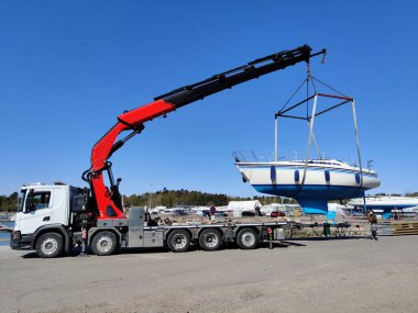 Finlandiya, Espoo 'daki Suomenoja limanında vinç tarafından çalınan bir yelkenli. Bir adam bir halat tutuyor, kayışı kaldırarak havada asılı duran tekneye rehberlik ediyor.