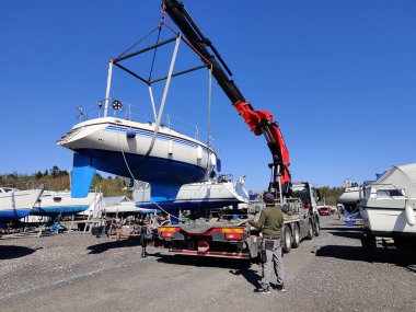 Finlandiya, Espoo 'daki Suomenoja limanında vinç tarafından çalınan bir yelkenli. Bir adam bir halat tutuyor, kayışı kaldırarak havada asılı duran tekneye rehberlik ediyor.
