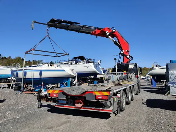 Finlandiya, Espoo 'daki Suomenoja limanında vinç tarafından çalınan bir yelkenli. Bir adam bir halat tutuyor, kayışı kaldırarak havada asılı duran tekneye rehberlik ediyor.