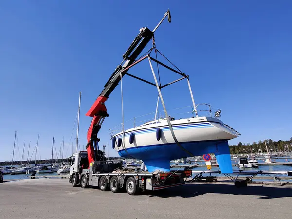Suomenoja, Espoo, Finlandiya 'da bir limanda vinç tarafından bir yelkenli kaldırılıyor. Ağır kaldırma kayışlarıyla havada asılı kalan gemi bakım ve mevsimsel depolama için hareket ediyor.