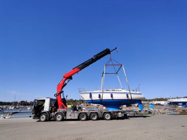 Suomenoja, Espoo, Finlandiya 'da bir limanda vinç tarafından bir yelkenli kaldırılıyor. Ağır kaldırma kayışlarıyla havada asılı kalan gemi bakım ve mevsimsel depolama için hareket ediyor.