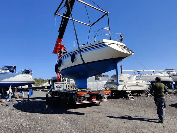 Finlandiya, Espoo 'daki Suomenoja limanında vinç tarafından çalınan bir yelkenli. Bir adam bir halat tutuyor, kayışı kaldırarak havada asılı duran tekneye rehberlik ediyor.