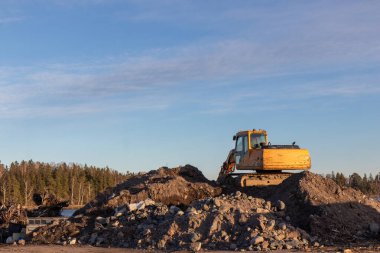 Günbatımında sarı kazıcı, mavi gökyüzünde inşaat alanında kazıcı. İnşaat alanı ve açık maden kazılarında ağır inşaat ekipmanları
