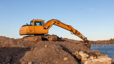 Günbatımında sarı kazıcı, mavi gökyüzünde inşaat alanında kazıcı. İnşaat alanı ve açık maden kazılarında ağır inşaat ekipmanları