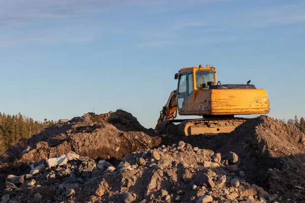 Günbatımında sarı kazıcı, mavi gökyüzünde inşaat alanında kazıcı. İnşaat alanı ve açık maden kazılarında ağır inşaat ekipmanları