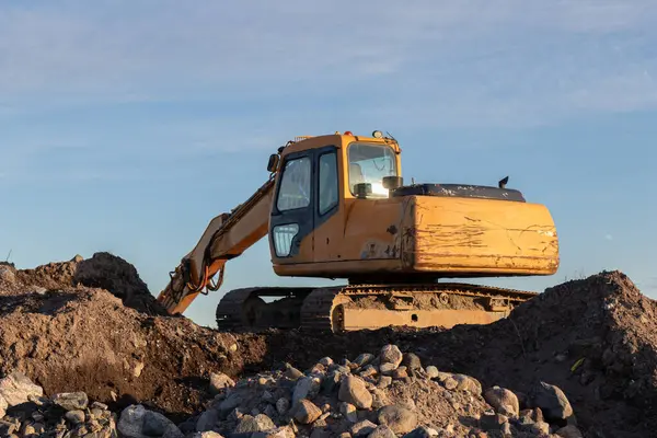 Günbatımında sarı kazıcı, mavi gökyüzünde inşaat alanında kazıcı. İnşaat alanı ve açık maden kazılarında ağır inşaat ekipmanları