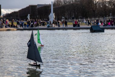 Paris, Fransa - 22 Şubat 2025: Lüksemburg Bahçesi 'ndeki (Jardin du Lüksemburg) merkez çeşmesinin etrafında toplanan çocuklar ve aileler, renkli yelkenli tekneleri denize indiriyorlar.