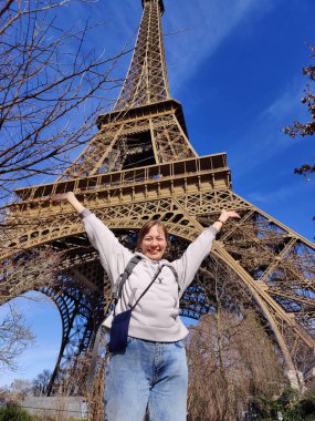 Paris, Fransa - 23 Şubat 2025: Mutlu bir bayan turist Paris 'teki Eyfel Kulesi' nin tabanında duruyor, güneşli bahar zamanı